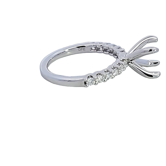 A silver-toned diamond engagement ring setting with a curved band and prong crown, featuring small clear stones along the band, shown on a plain white background.