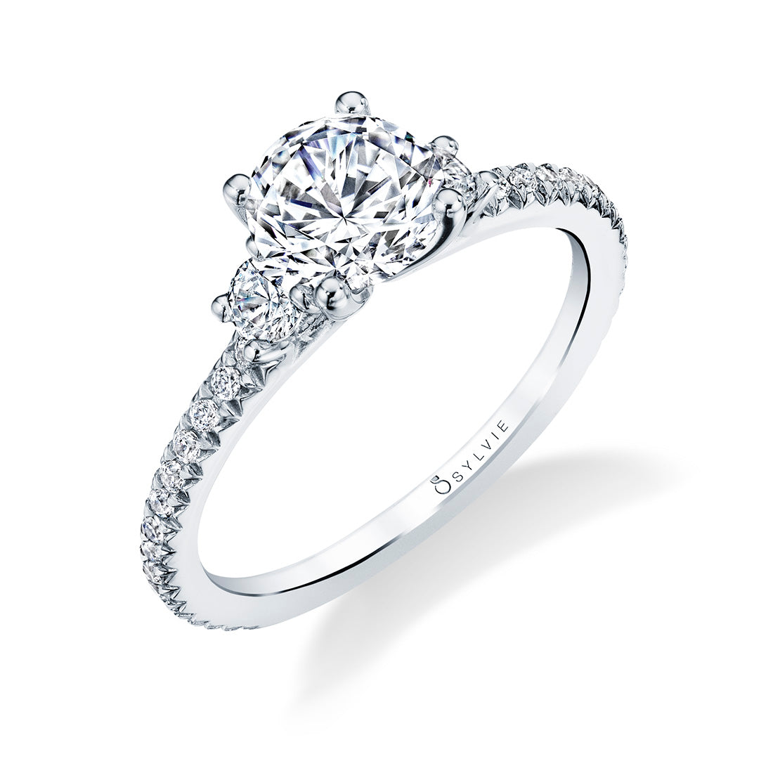 Sylvie Collection .35ctw Diamond Semi-Mount in 14k White Gold. This delicate three stone engagement ring features a beautiful 1 carat round center in a prong setting. The shank includes shimmering, cascading round-cut diamonds on both sides of the band, bringing the band's total weight to 0.39 carats.  A semi-mount engagement ring is a diamond mounting that lacks the center stone. Center stones are purchased and priced separately.